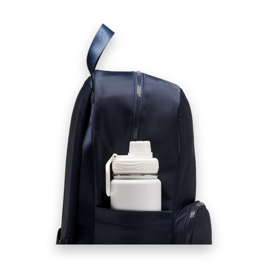 A close-up of a navy blue backpack with a front pocket holding a white insulated water bottle, shown against a light gray studio background.