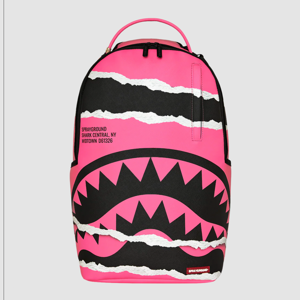 A Sprayground Shark backpack in vibrant pink and black, featuring a shark mouth graphic with white torn-paper accents, shown against a light gray background.