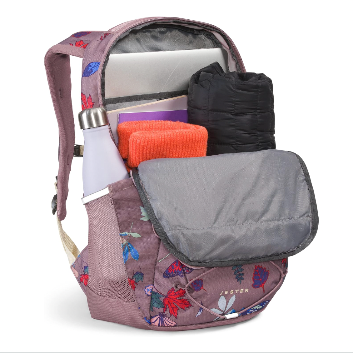 A pinkish-purple backpack with a floral print, shown open with its laptop compartment, side pocket, and front organizer pocket displayed. The bag contains a laptop, a black puffer bag, an orange towel, and a white bottle.